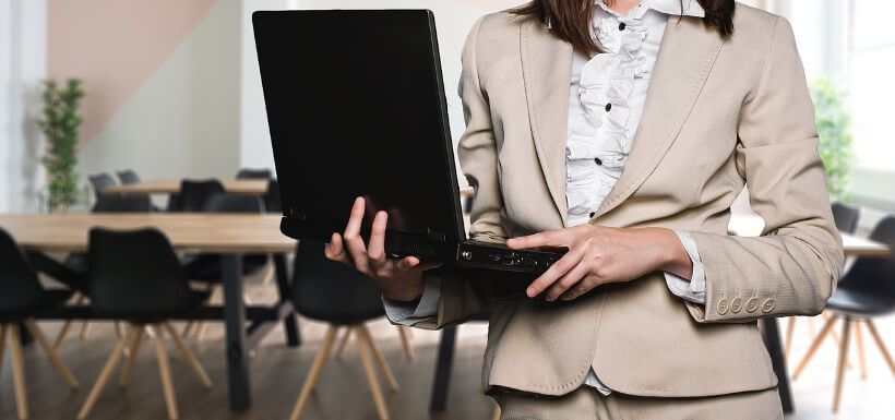 Geschäftsfrau steht mit Laptop in der Hand vor einem noch leeren Meeting-Raum