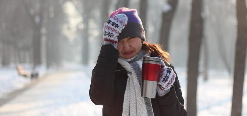 junge Frau in verschneitem Park packt sich an den Kopf