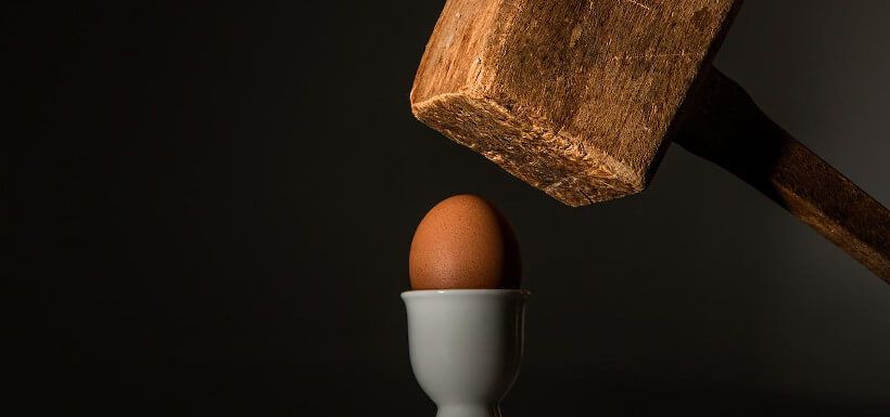 ein großer Holzhammer schwebt kurz vor dem Schlag auf ein Ei