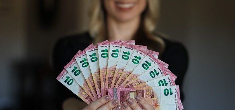 Frau hält lächelnd einen vollen Fächer Geldscheine (10 EUR) in die Kamera
