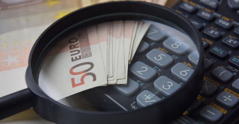Euro-Scheine und Lupe mit Taschenrechner als Symbol für Geld sparen