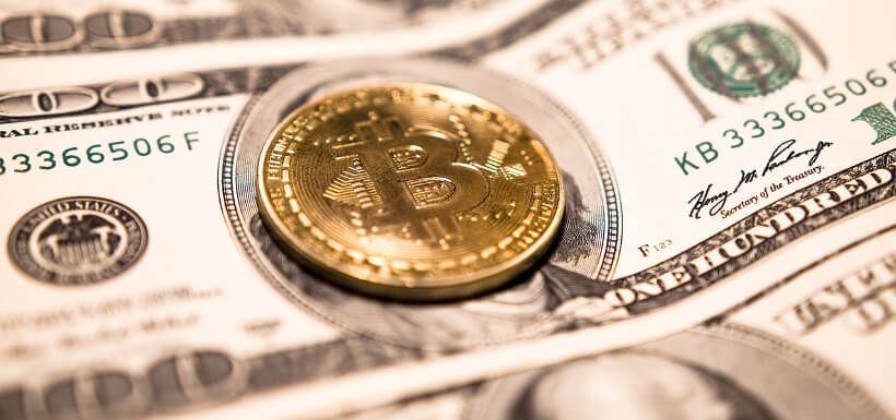 eine Bitcoin-Münze liegt auf einem Stapel Dollarscheine