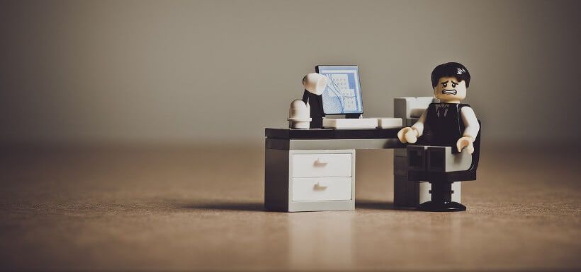 Legofigur: ein Mann im Anzug sitzt an einem Schreibtisch und sieht sehr unglücklich aus