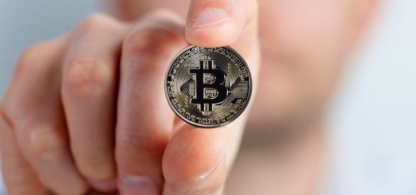 Nahaufnahme einer Hand, die eine Bitcoin-Münze hält