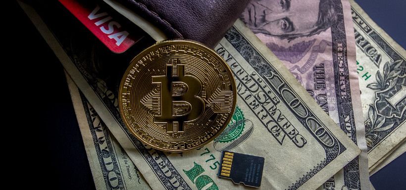 ein physischer Bitcoin und ein Computerchip liegen auf einem prallen Geldbeutel