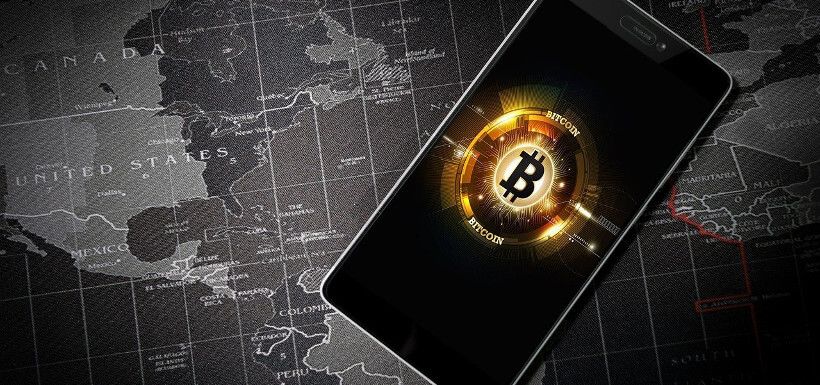 ein Smartphone, auf dem ein Bitcoin-Symbol zu sehen ist, liegt auf einer Weltkarte