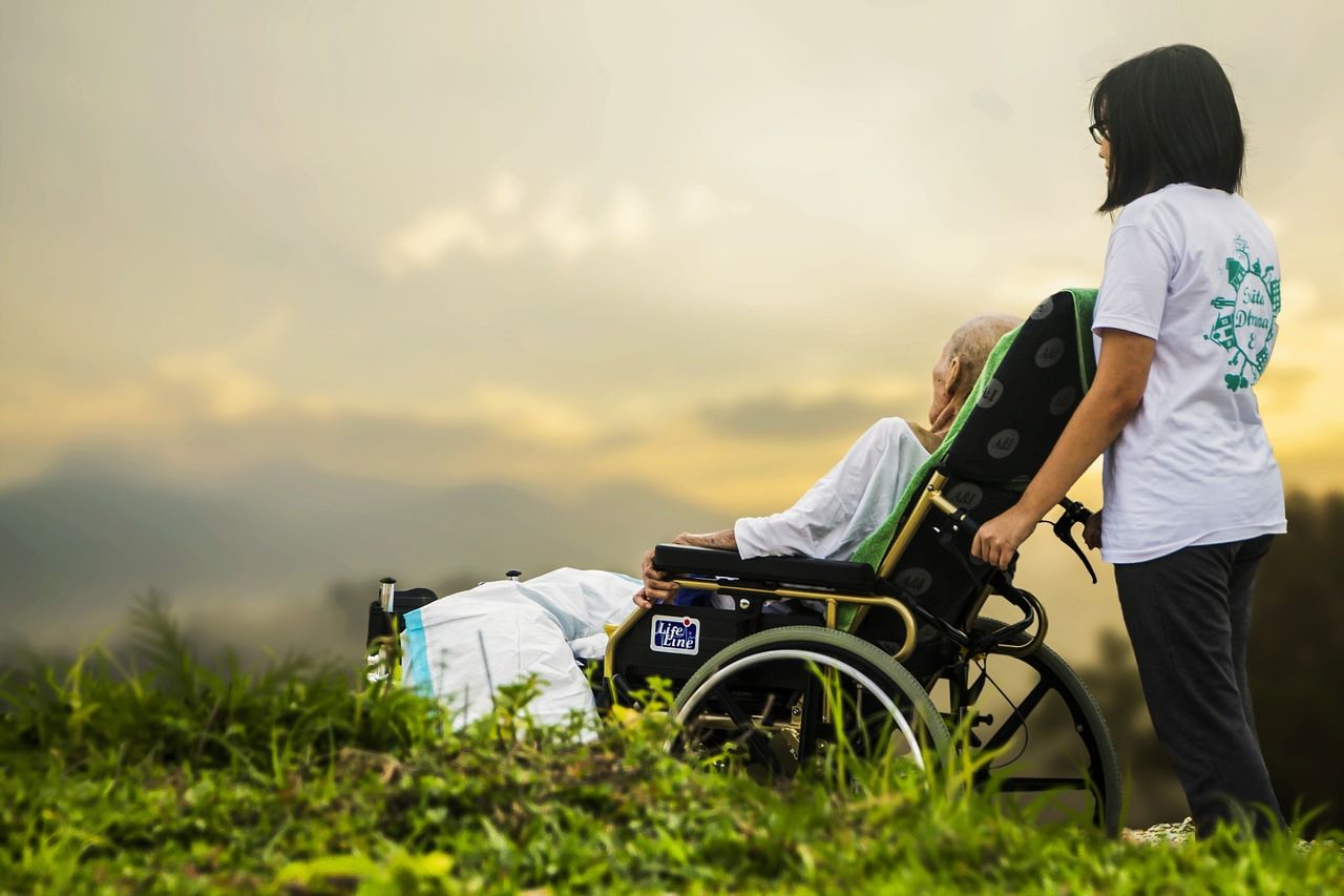Frau als Pflegekraft mit Dame im Rollstuhl