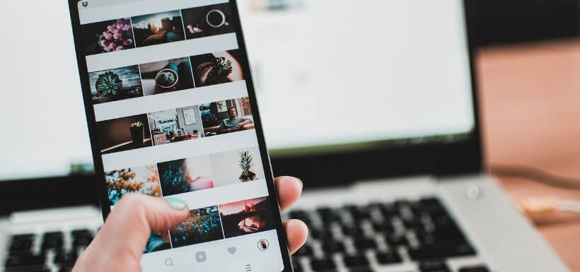 Smartphone in Hand vor Laptop in HG, zeigt Instagram