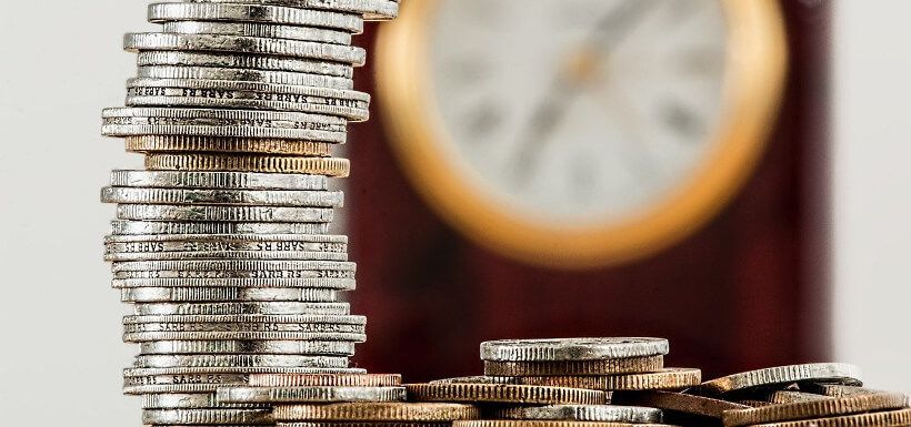 Symbolbild Investement: im VG ein Münzstapel, im HG eine Uhr